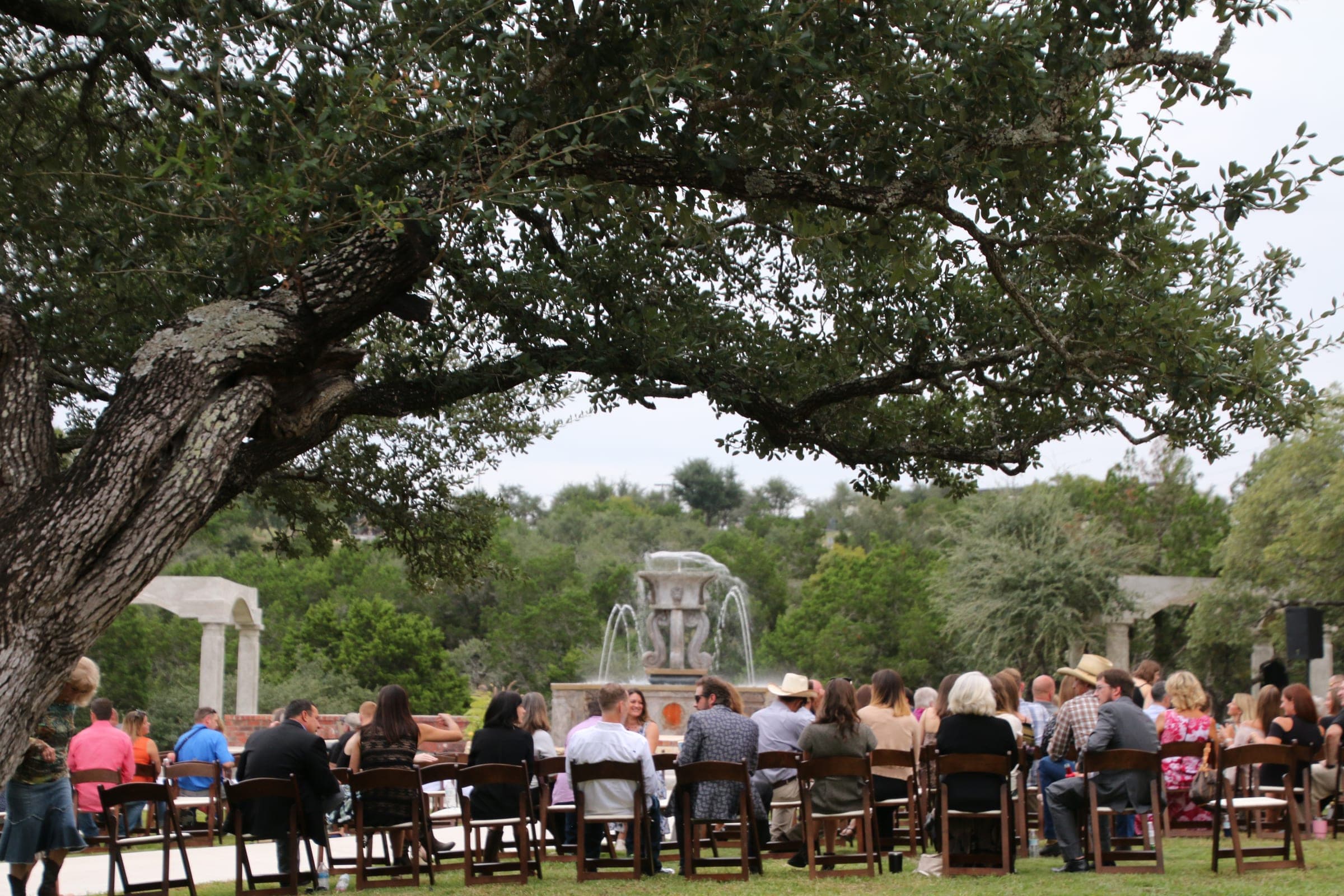 Guests seated for an outdoor ceremony beneath the oaks